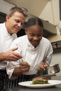 Chef Instructing Trainee In Restaurant Kitchen